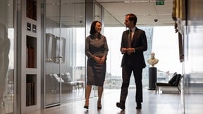 Two colleagues walking through a light-filled office lobby with large windows and views of the City of London.